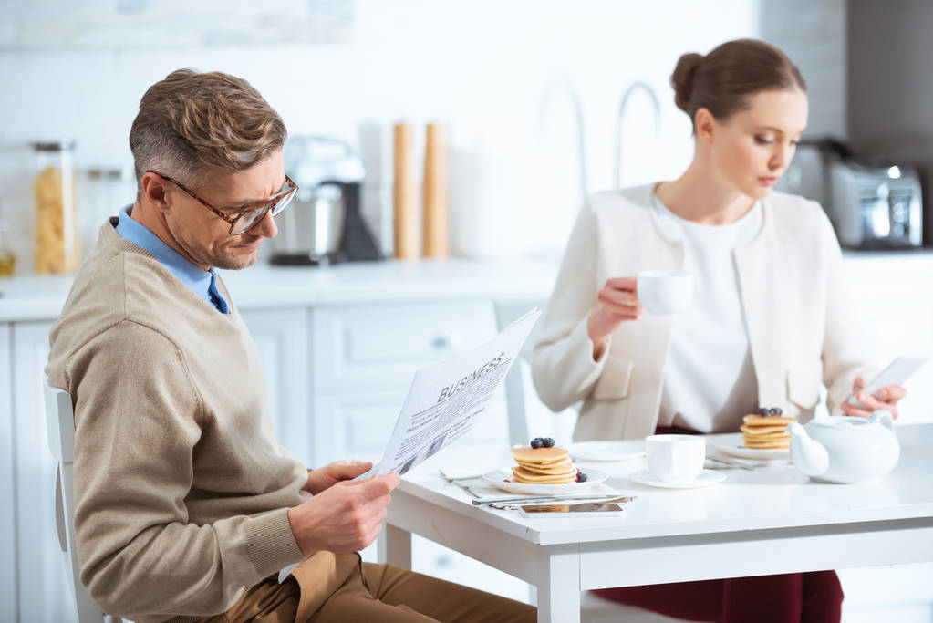 adult couple reading newspaper, drinking tea and ignoring each other during breakfast in morning - Photo, Image