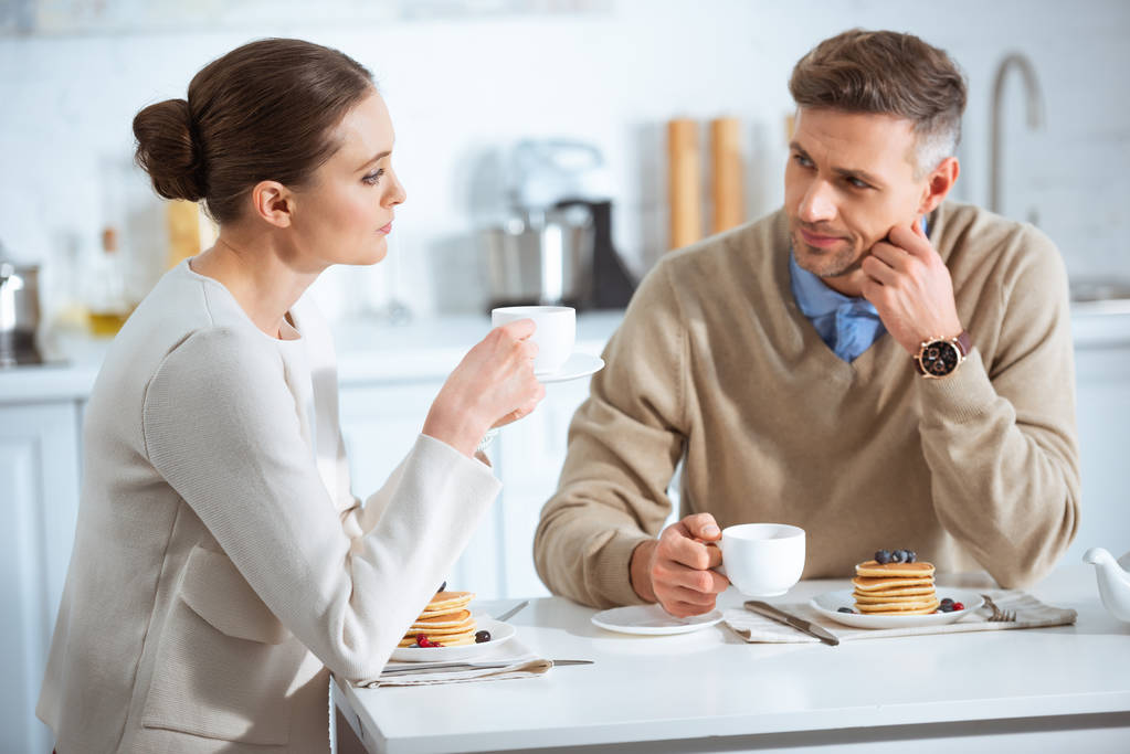 selective focus of dissatisfied adult couple sitting at table while having breakfast in morning - Zdjęcie, obraz