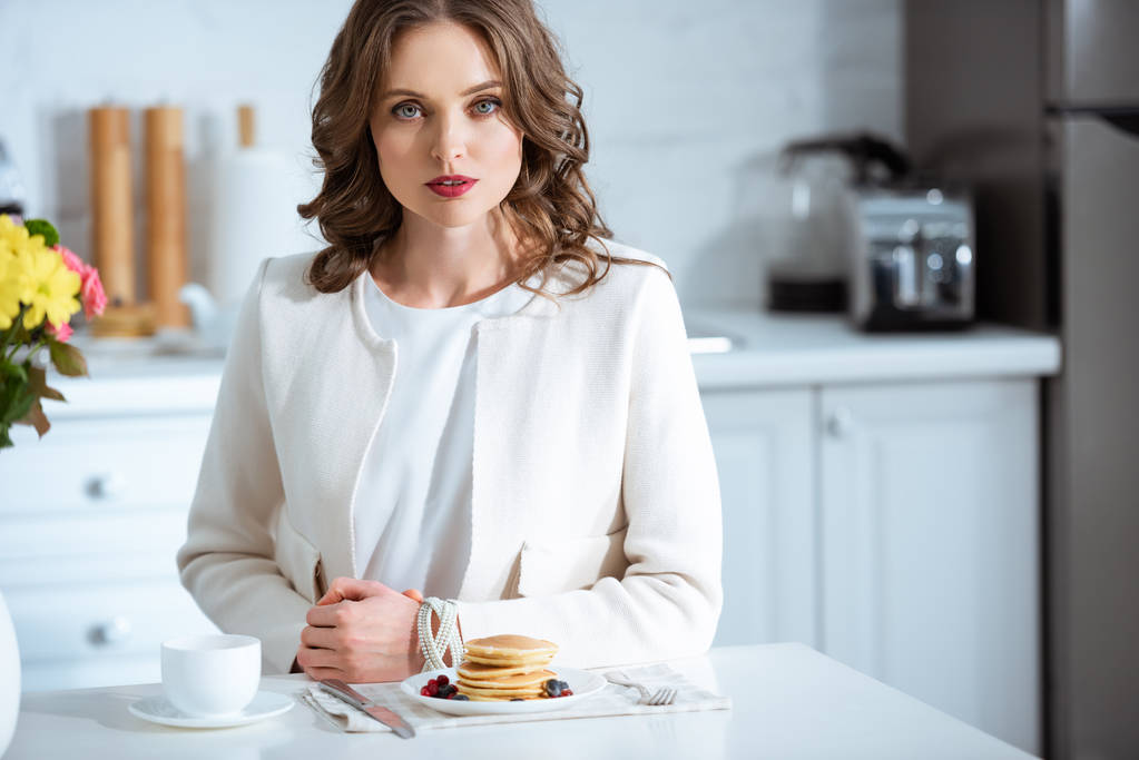 beautiful woman sitting at table with pancakes and coffee during breakfast in kitchen - Photo, Image