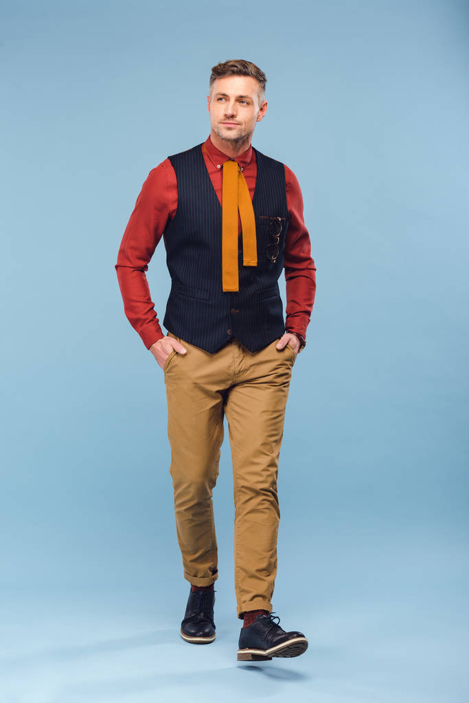 schöner stilvoller Mann in formeller Kleidung mit Händen in Taschen auf blauem Hintergrund - Foto, Bild
