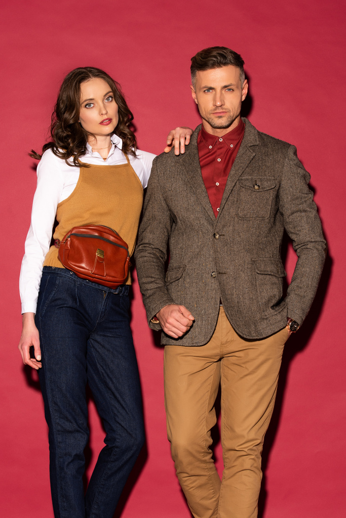 atractiva pareja de moda en ropa formal mirando a la cámara y posando sobre fondo rojo
 - Foto, imagen
