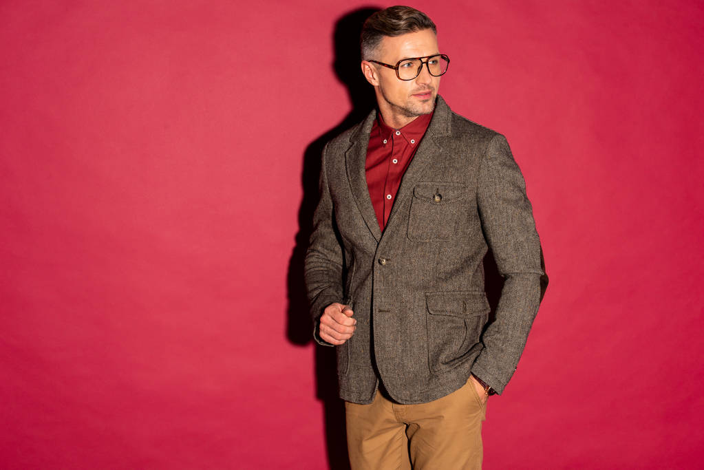 selbstbewusster stilvoller Mann in formaler Kleidung und Brille auf rotem Hintergrund mit Kopierraum - Foto, Bild