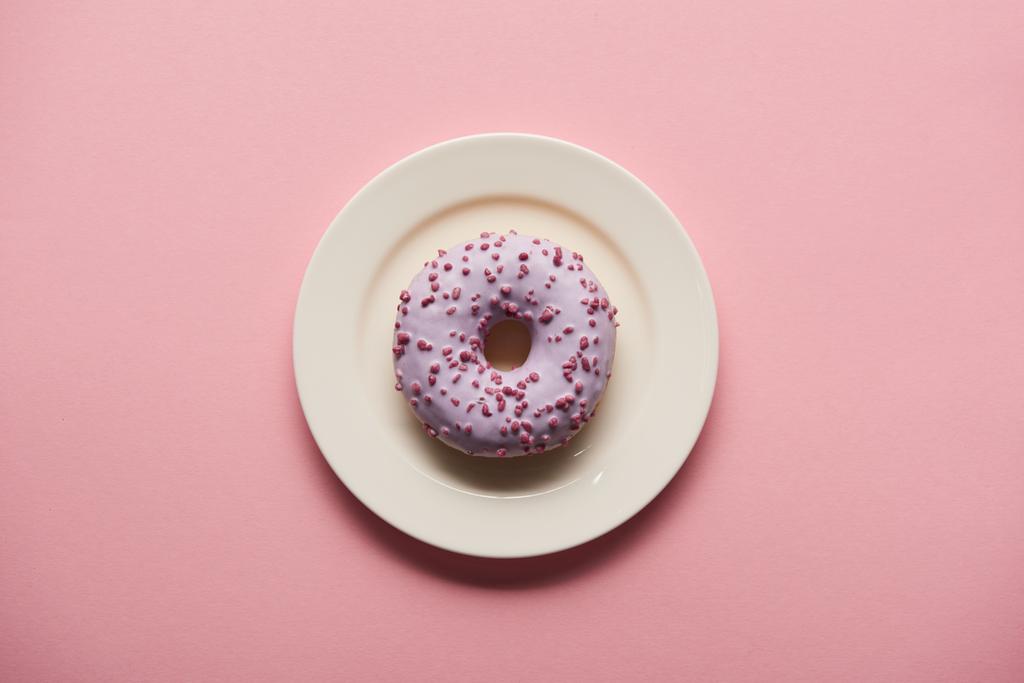 bovenaanzicht van smakelijke donut op witte plaat op roze achtergrond - Foto, afbeelding