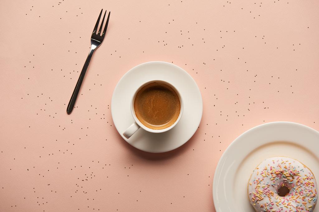 вид сверху на сладкий пончик рядом с чашкой кофе и вилкой на розовом фоне
 - Фото, изображение