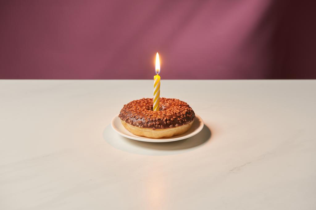 brandende kaars in het midden van de donut met slagroom en hagelslag op witte tafel  - Foto, afbeelding
