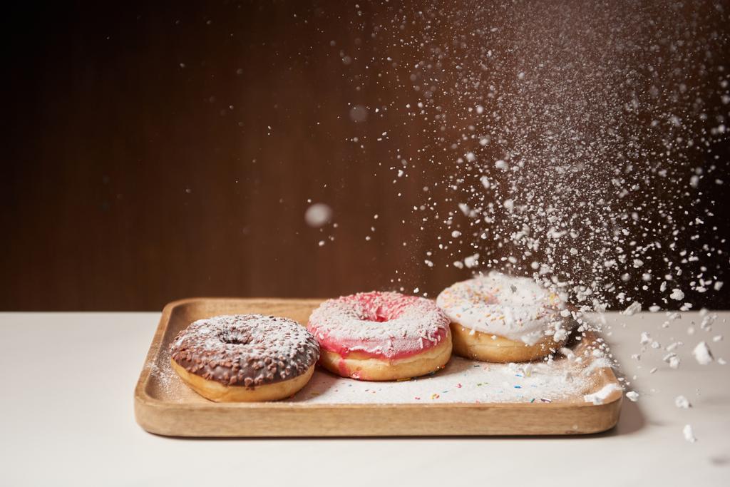 zoete donuts met zeven van suiker poeder op houten snijplank - Foto, afbeelding