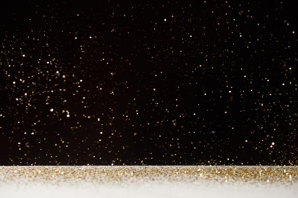 selectieve aandacht van gouden sparkles vallen op witte tafel geïsoleerd op zwart  - Foto, afbeelding