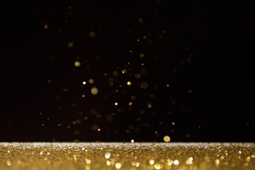 selective focus of bright golden sparkles on table isolated on black  - Foto, afbeelding