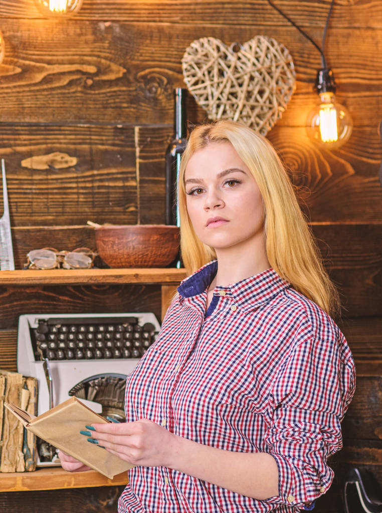 Girl reading book in house of gamekeeper. Girl in casual outfit in wooden vintage interior enjoy poetry. Lady blonde on calm face in plaid clothes holds book, reading poetry. Vintage concept - Photo, Image