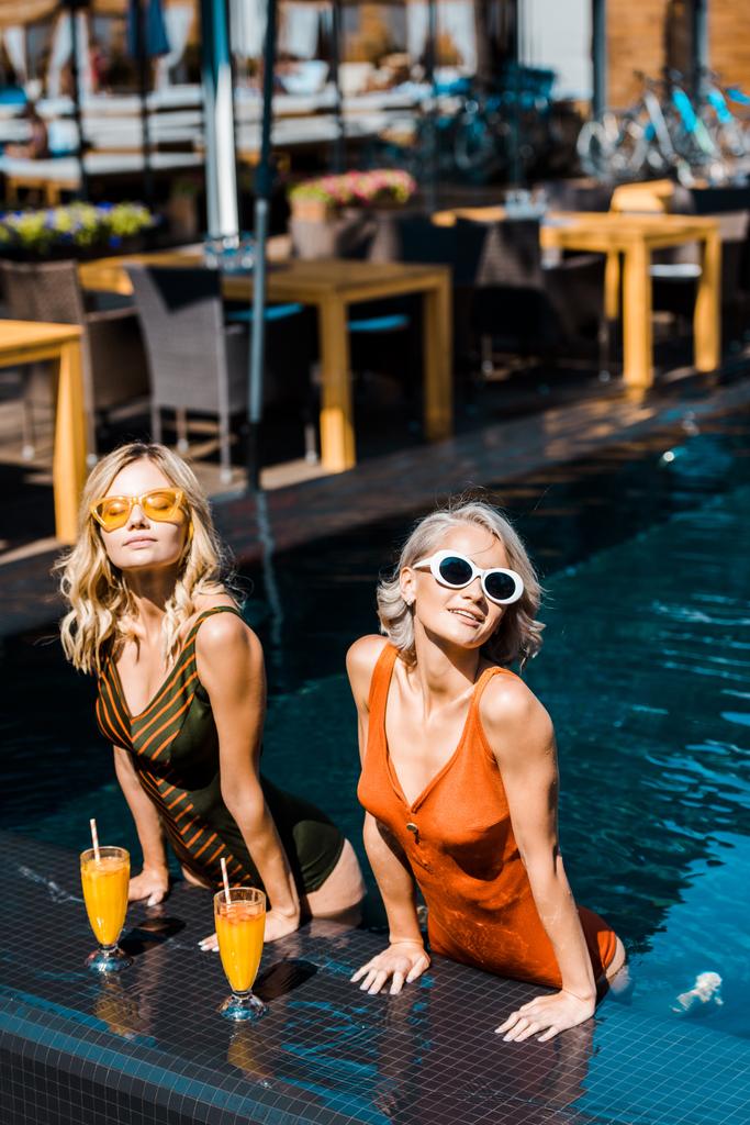 stijlvolle meisjes ontspannen in het zwembad met cocktails - Foto, afbeelding