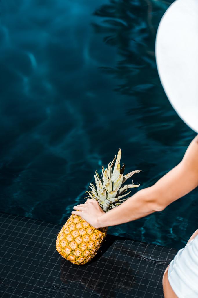 Teilbild einer Frau, die mit süßer Ananas in der Nähe des Swimmingpools posiert - Foto, Bild
