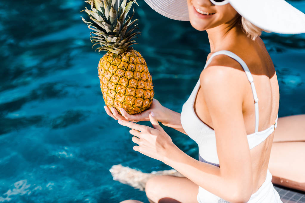 przycięte widok kobiety w strojach kąpielowych, pozowanie z ananasem w pobliżu basenu - Zdjęcie, obraz