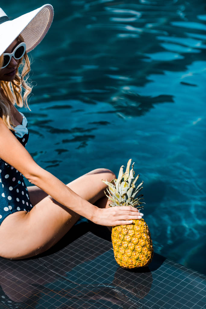молодая женщина в купальниках позирует с ананасом возле бассейна
 - Фото, изображение