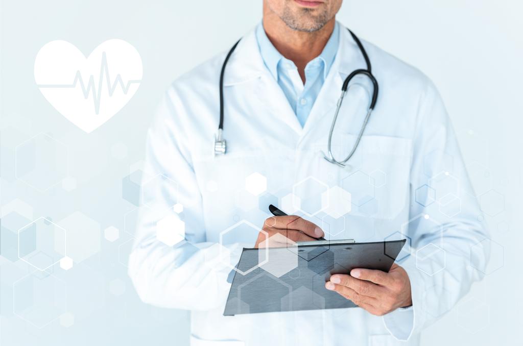 bijgesneden afbeelding van arts met de stethoscoop op schouders iets schrijven in Klembord op wit met hartslag en medische interface - Foto, afbeelding