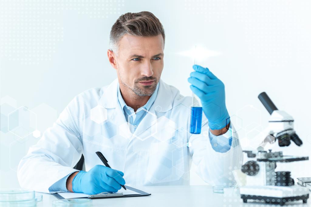 handsome scientist looking at test tube with blue reagent  - Photo, Image