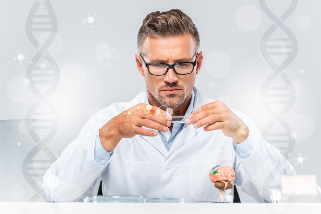 handsome scientist in glasses looking at reagent with dna symbols - Photo, Image