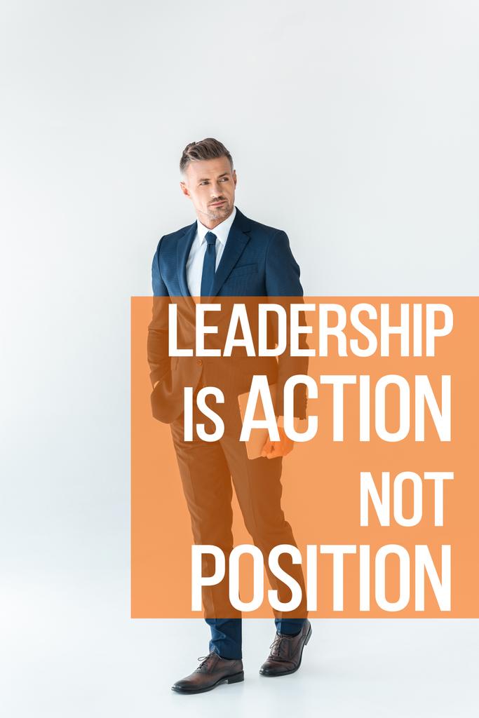 красивый бизнесмен стоит с ноутбуком и смотрит в сторону изолированных на белом с надписью "лидерство - это действие, а не позиция"
   - Фото, изображение