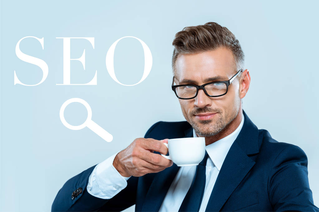schöner Geschäftsmann, der Kaffee trinkt und in die Kamera schaut, isoliert auf blauem Grund mit SEO-Zeichen - Foto, Bild