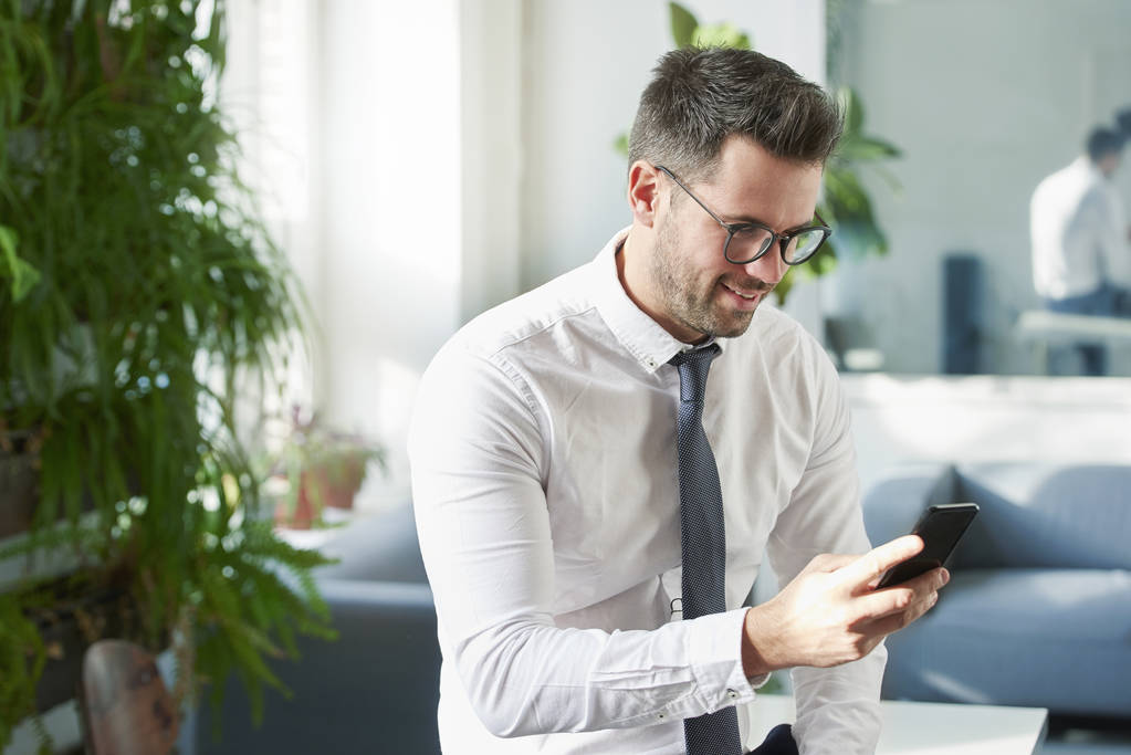 Ritratto di uomo d'affari che utilizza il suo telefono cellulare e SMS mentre è seduto in ufficio
.  - Foto, immagini