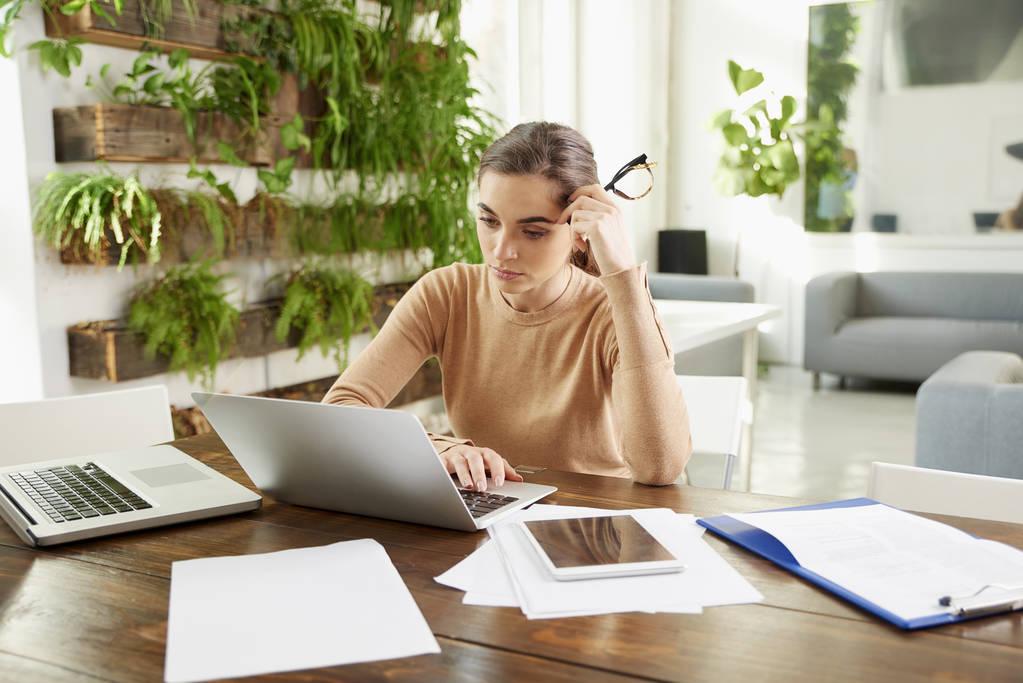 Знімок молодої бізнес-леді виглядає задумливо, сидячи в ноутбуці і працюючи в офісі
.  - Фото, зображення