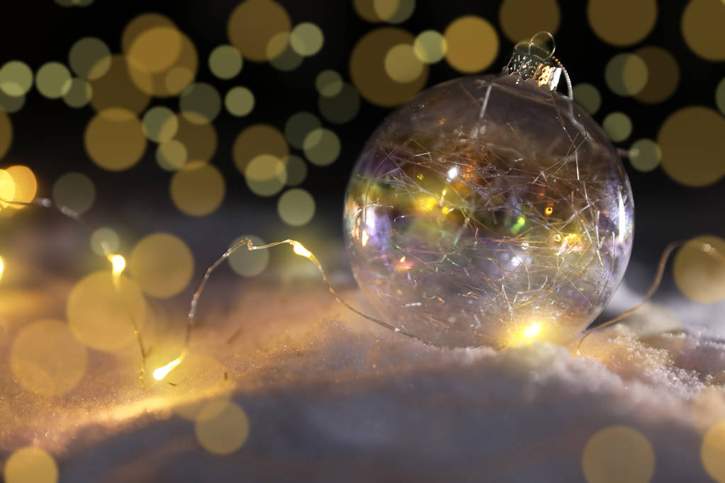 Kerst bal en gloeiende lichten op sneeuw tegen onscherpe achtergrond, ruimte voor tekst. Winter decor - Foto, afbeelding