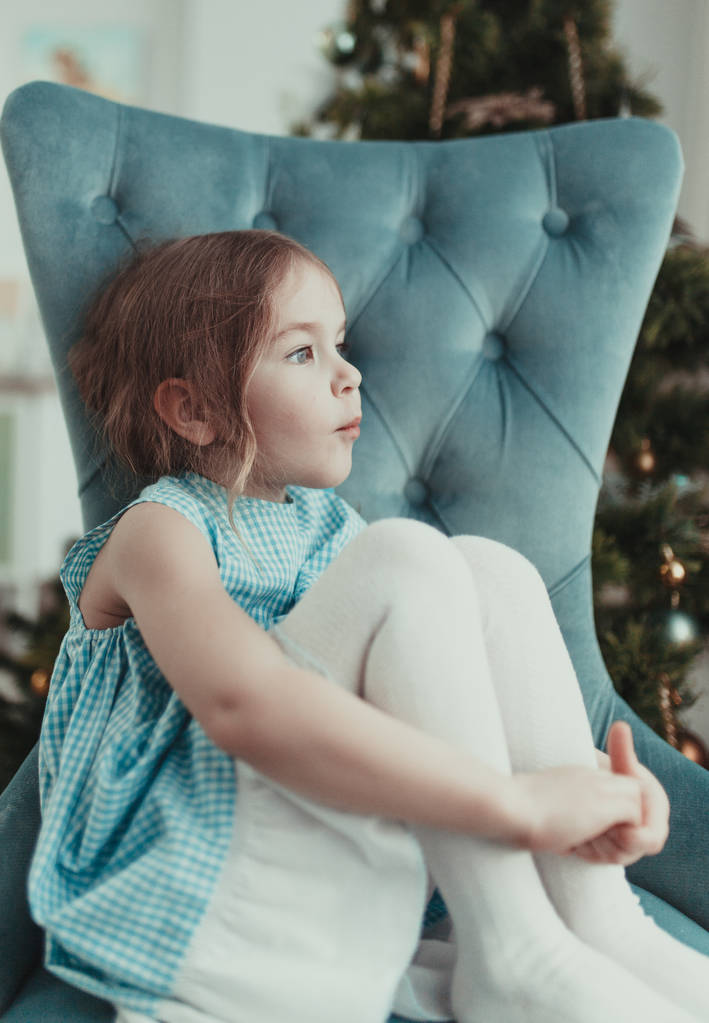 Досить задумливою маленька дівчинка, що сидить у крісло поблизу Різдво дерево. критий - Фото, зображення