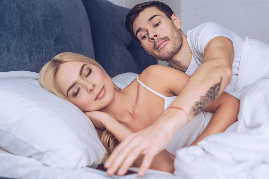 suspicieux jeune homme atteindre pour smartphone tandis que belle petite amie dormir dans le lit, concept de méfiance
 - Photo, image