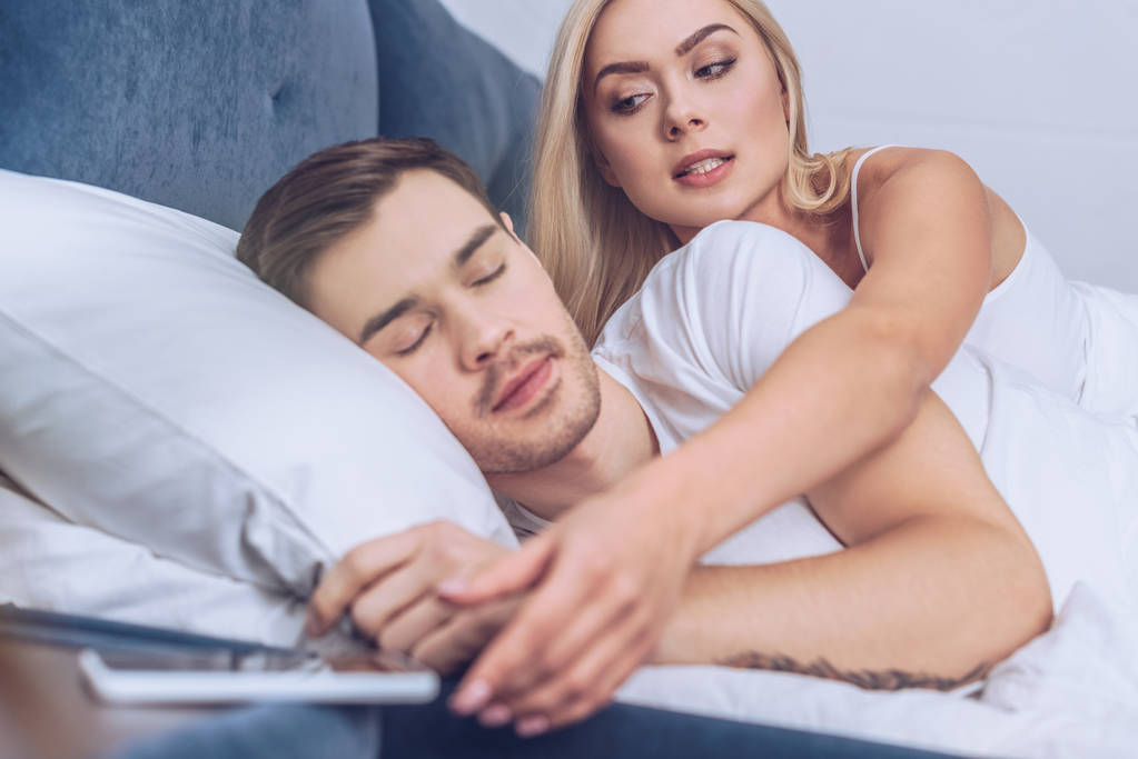 mujer celosa alcanzar para el teléfono inteligente mientras el novio durmiendo en la cama
   - Foto, Imagen