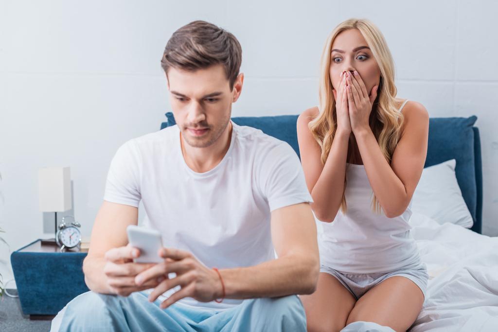 Schockierte junge Frau sieht Freund mit Smartphone im Bett an, misstraut Konzept - Foto, Bild