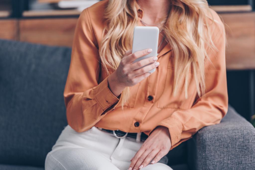 Schnappschuss einer jungen blonden Frau, die auf der Couch sitzt und ihr Smartphone benutzt - Foto, Bild