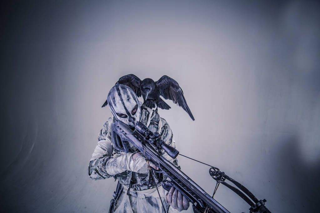 ritratto dell'uomo cacciatore in mimetizzazione con balestra e corvo in posa su sfondo grigio
 - Foto, immagini