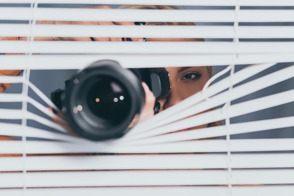 close-up view of camera and young woman taking pictures and spying through blinds  - Photo, Image