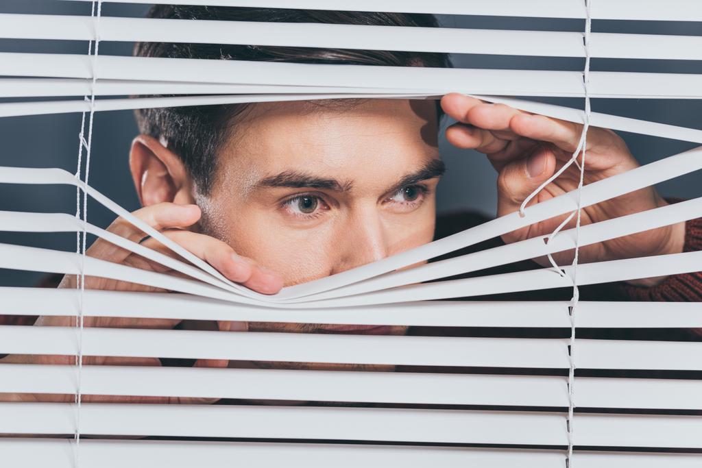 verdachte jongeman op zoek weg via blinds, spioneren concept - Foto, afbeelding