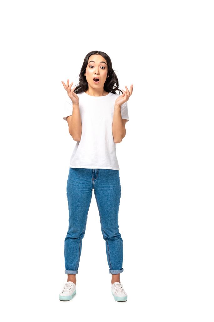 шокована азіатська жінка в білій футболці і синіх джинсах, що стоять з піднятими руками ізольовані на білому
  - Фото, зображення
