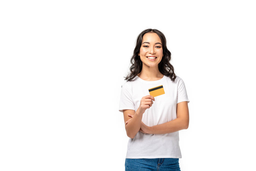 Sorrindo asiático jovem mulher em branco t-shirt segurando cartão de crédito isolado no branco
 - Foto, Imagem