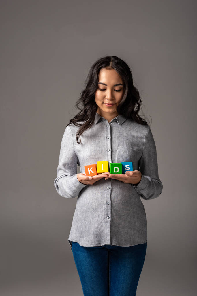 Sonriendo embarazada joven asiática sosteniendo alfabeto cubos con palabra niños aislados en gris
 - Foto, imagen
