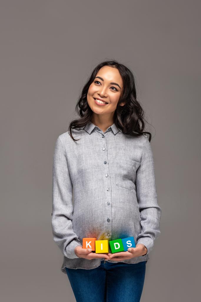 Sonriendo embarazada asiática mujer sosteniendo alfabeto cubos con palabra niños aislado en gris
 - Foto, Imagen