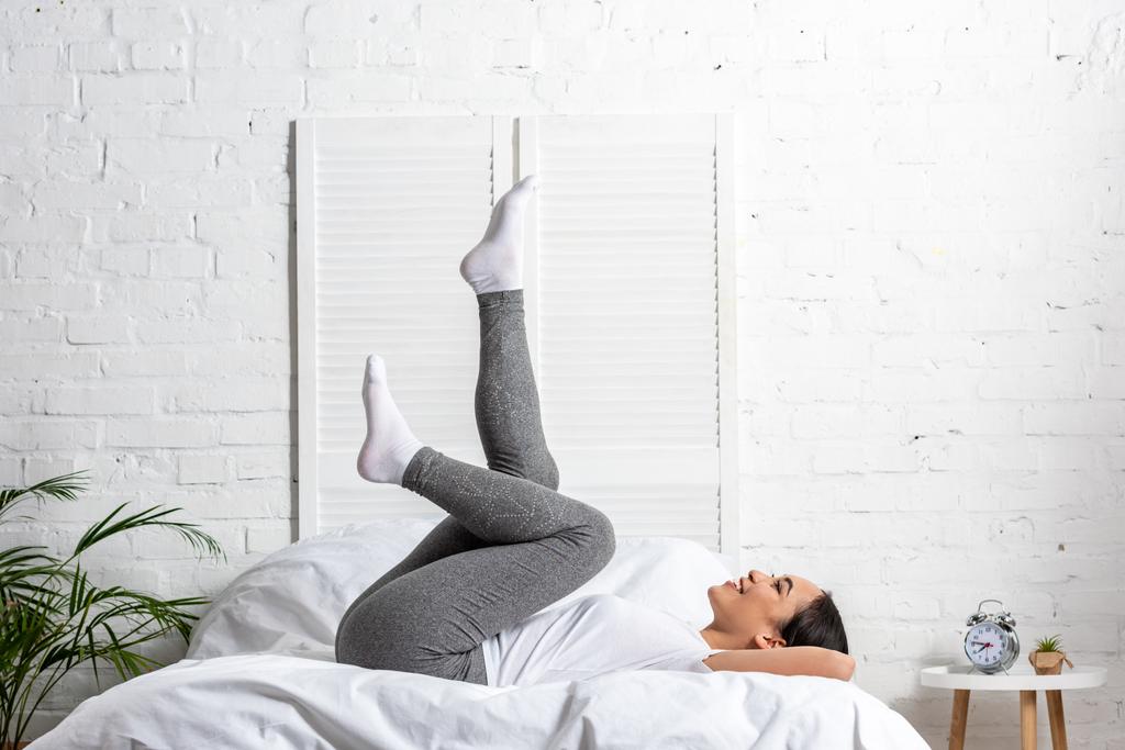 Aziatische vrouw in wit t-shirt en grijze legging doen oefeningen in bed - Foto, afbeelding