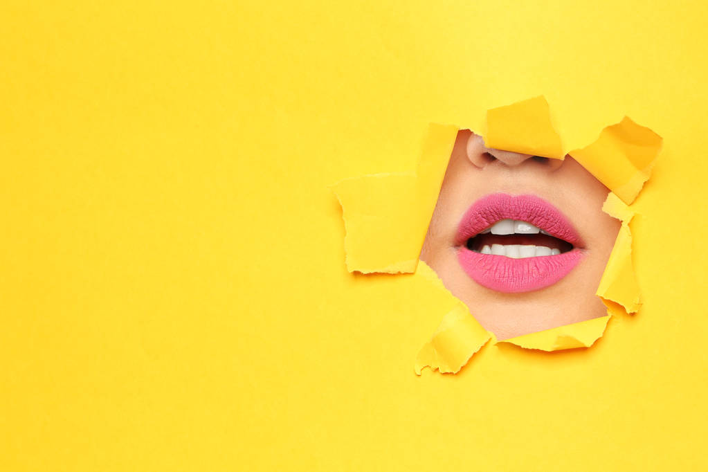 Lippen van jonge vrouw met prachtige lippenstift zichtbaar door gat in kleur papier. Ruimte voor tekst - Foto, afbeelding