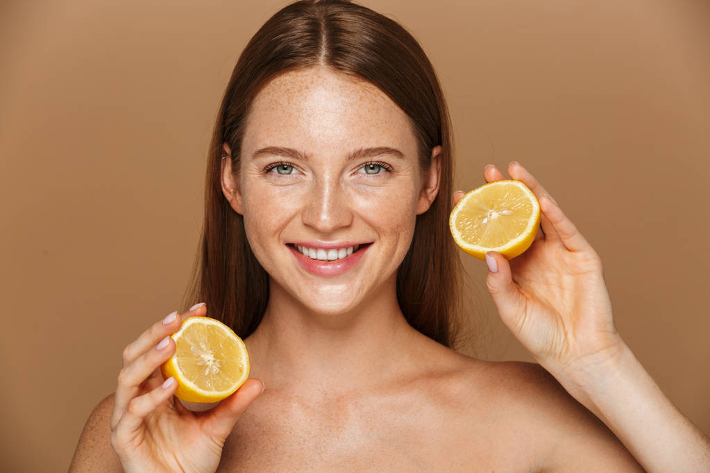 Beauty image of pretty shirtless woman with long hair holding two pieces of orange isolated over beige background - Photo, Image
