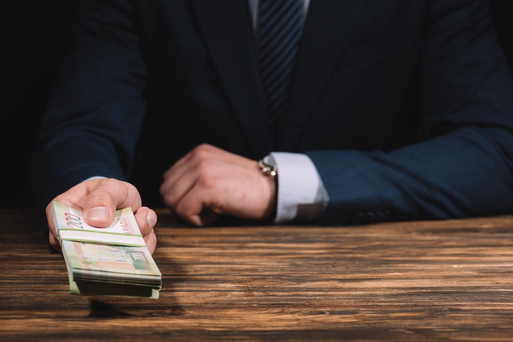 обрезанный снимок бизнесмена в костюме с российскими рублями банкнотами в руке над деревянным столом
 - Фото, изображение