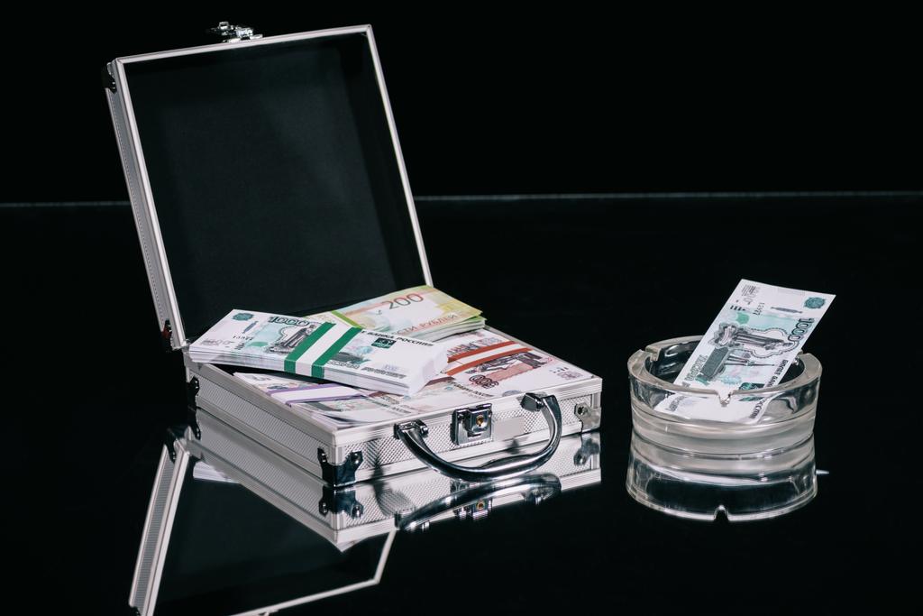 roubles russes billets en valise coffre-fort et de l'argent dans le cendrier sur noir
  - Photo, image