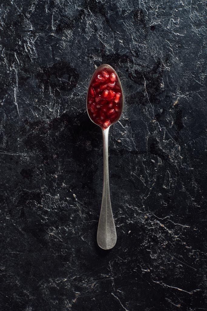 Top näkymä lusikka granaattiomena siemenet tummalla pinnalla
 - Valokuva, kuva