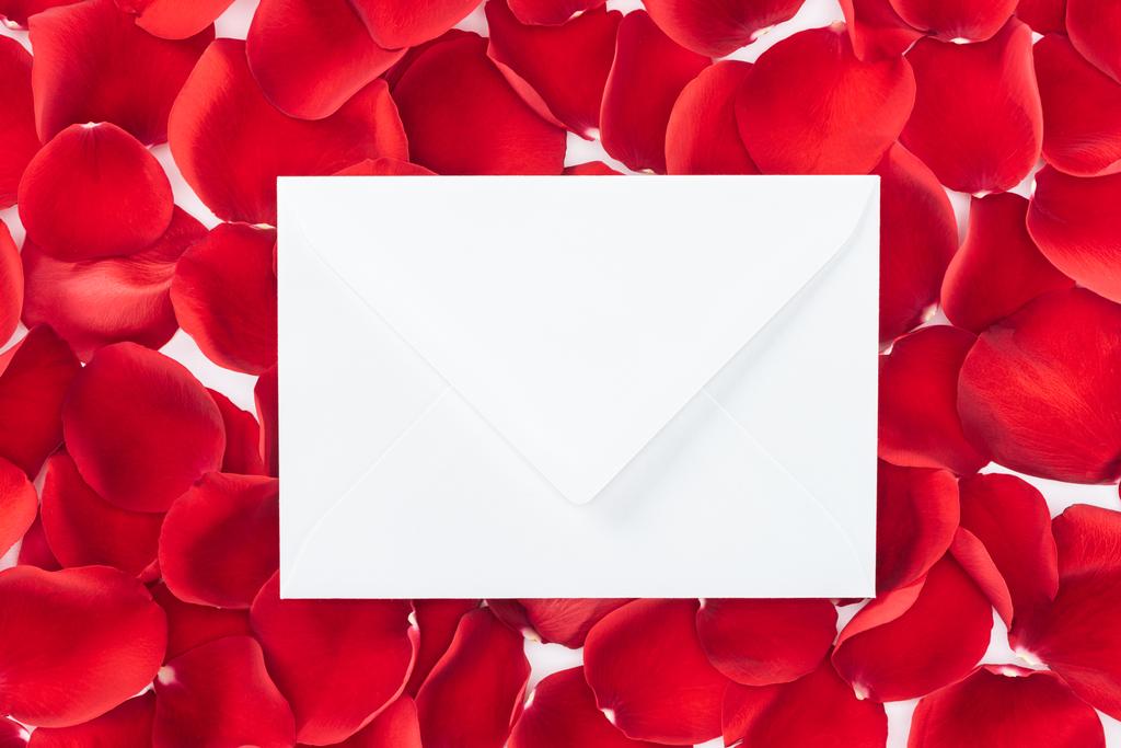 bovenaanzicht van envelop met kopie ruimte en rode rozenblaadjes op achtergrond - Foto, afbeelding
