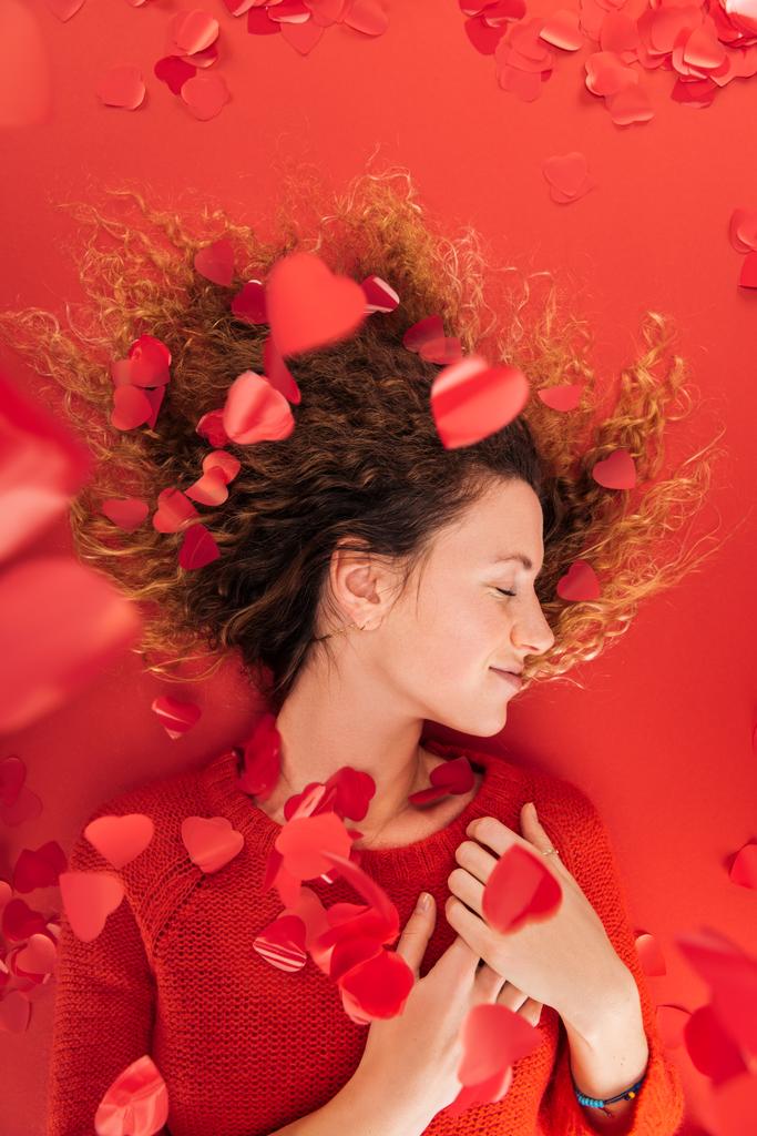top view of girl and falling heart shaped confetti isolated on red, st valentines day concept - Photo, Image