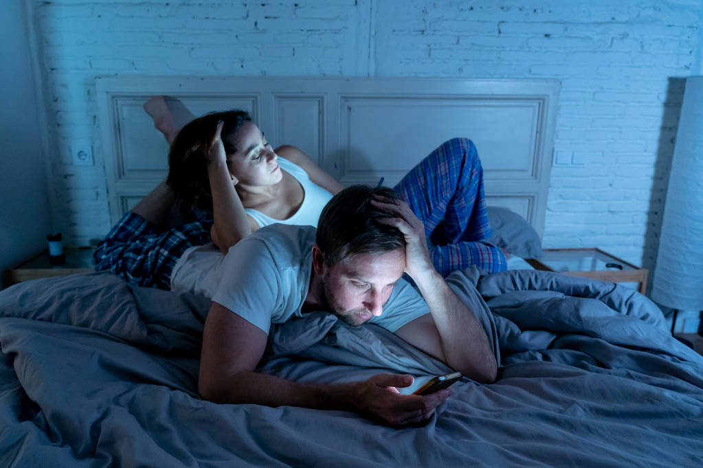 Triste coppia di uomini e donne sposati che usano il loro smartphone intelligente a letto di notte ignorandosi a vicenda come estranei nei problemi di relazione e comunicazione e nella dipendenza da internet sui social network
. - Foto, immagini
