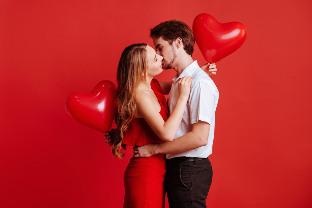 Ritratto di attraente giovane coppia in posa su sfondo rosso e tenendo palloncini cuore
. - Foto, immagini
