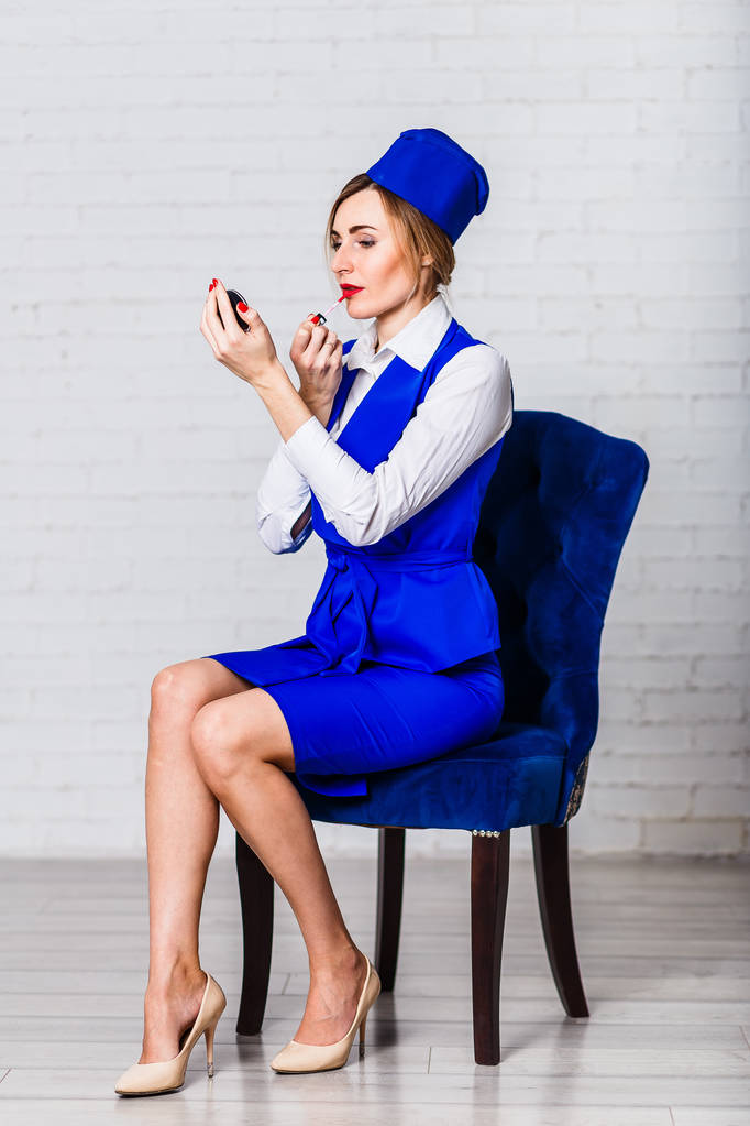 női stewardess festék ajkak. Szexi fiatal nő ül a kék szék, fehér alapon kék stewardess jelmez - Fotó, kép