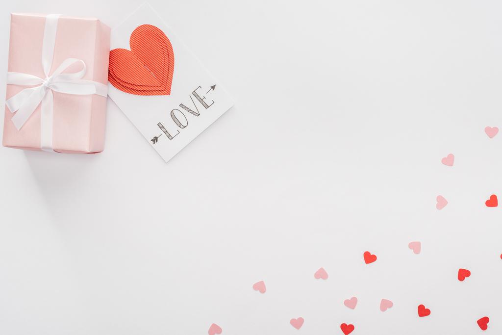 Draufsicht auf Geschenkbox, Papierherzen und Grußkarte mit "Liebe" Schriftzug isoliert auf weißem, Valentinstag-Konzept - Foto, Bild