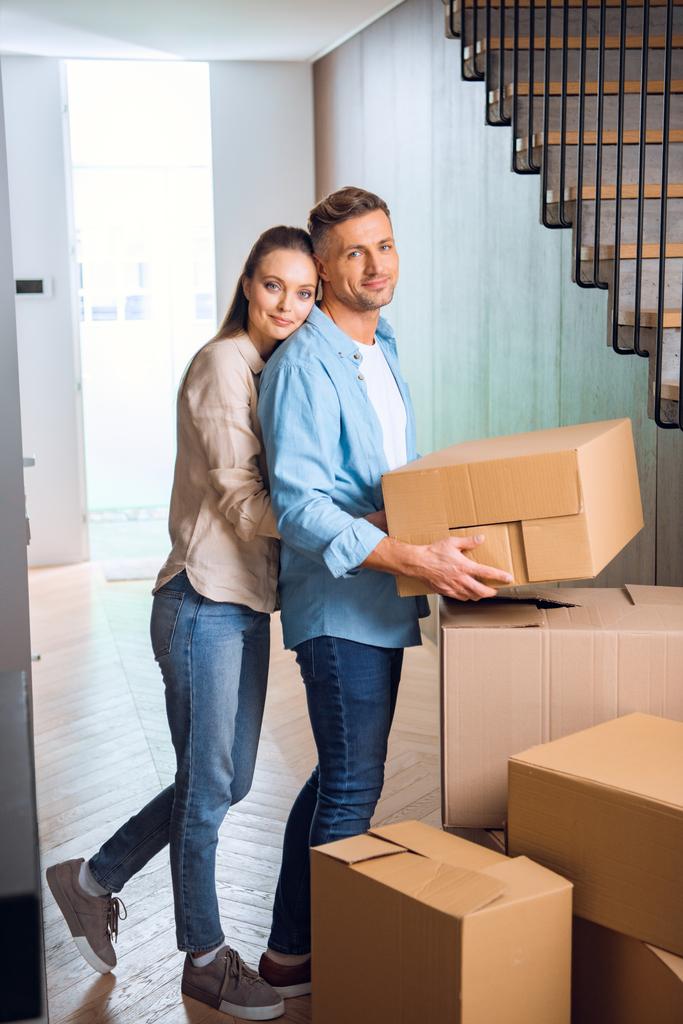 happy woman hugging handsome husband with box in hands  in new home  - Photo, Image